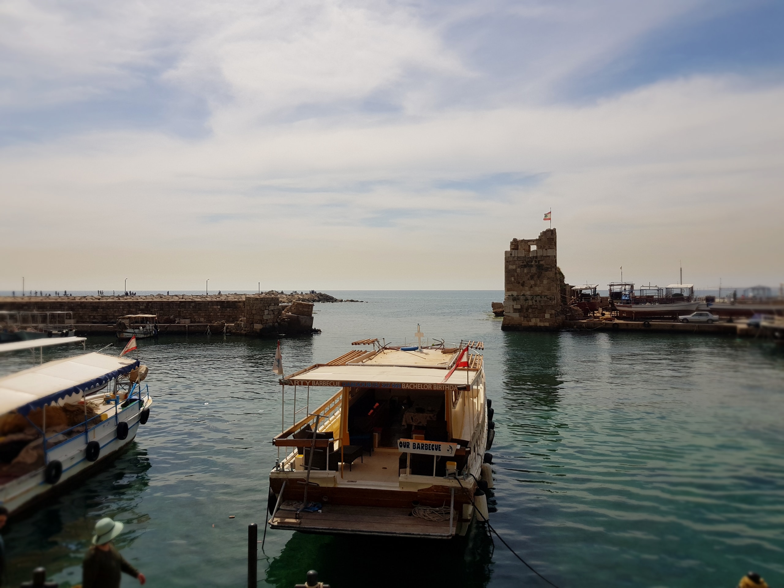 Small boats moored in a harbour with an old stone fort on the breakwater