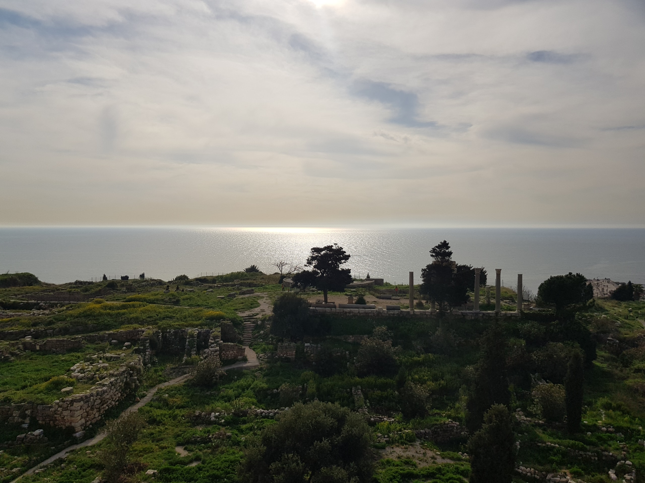 Green hillside of ruins looking out over the sea beneath a wide cloudy sky