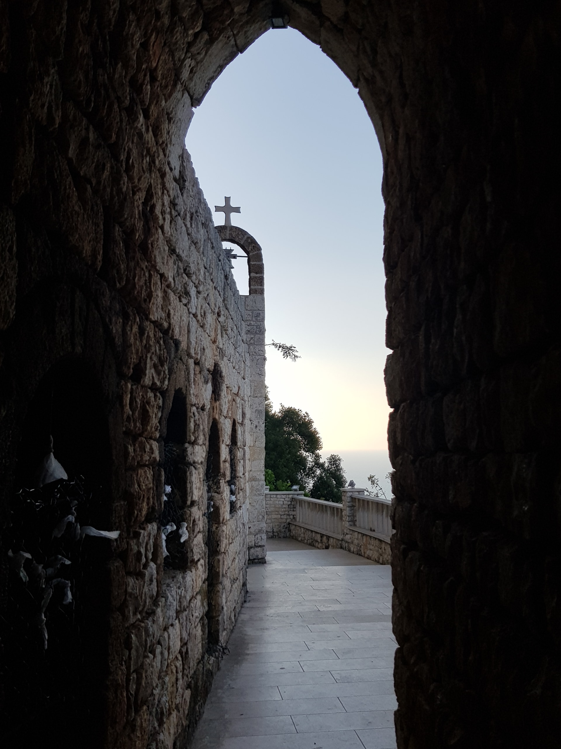 Stone archway framing a narrow passage and a small church bell tower