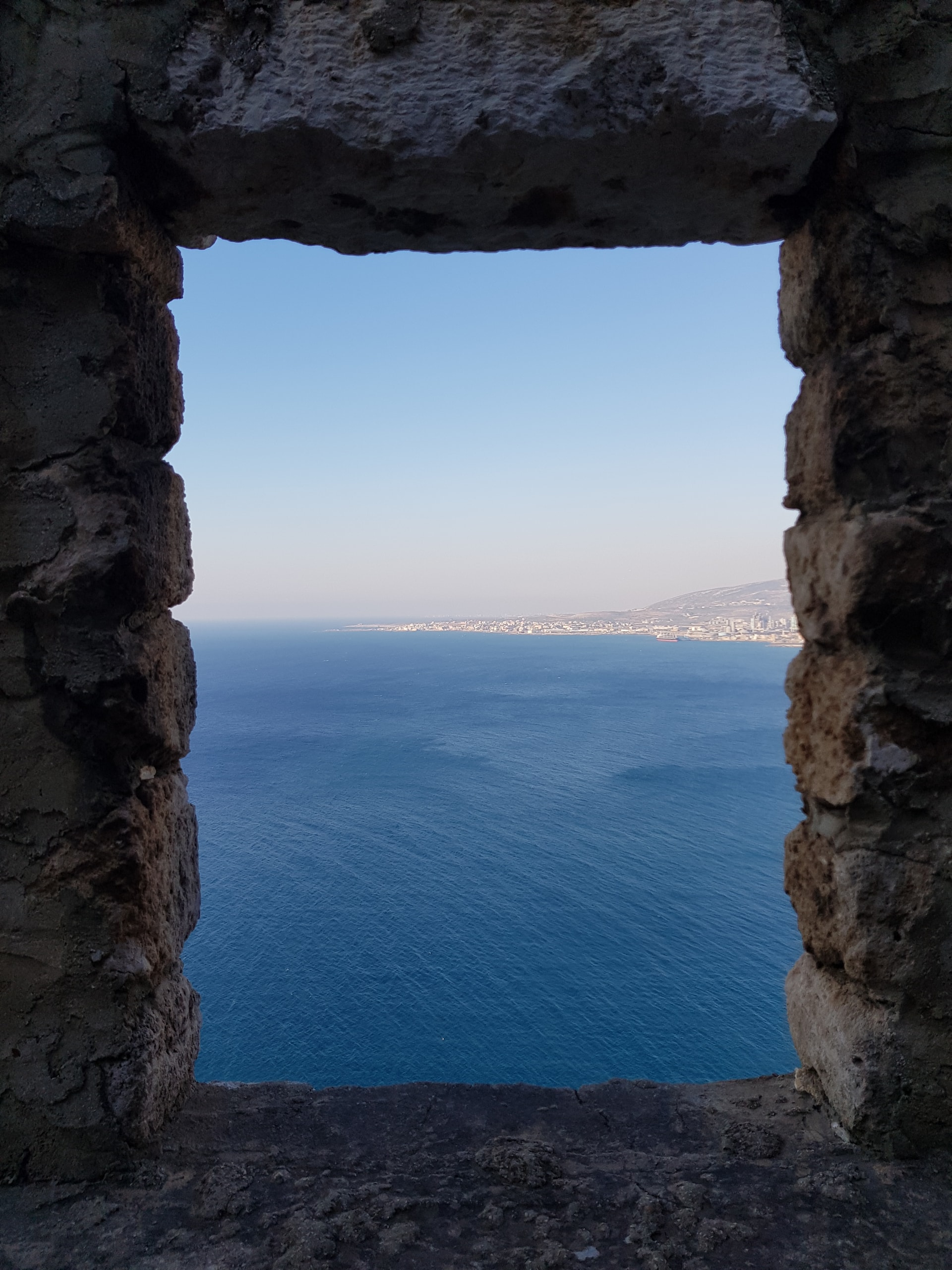 Rough stone window opening onto a deep blue sea and a distant coastline