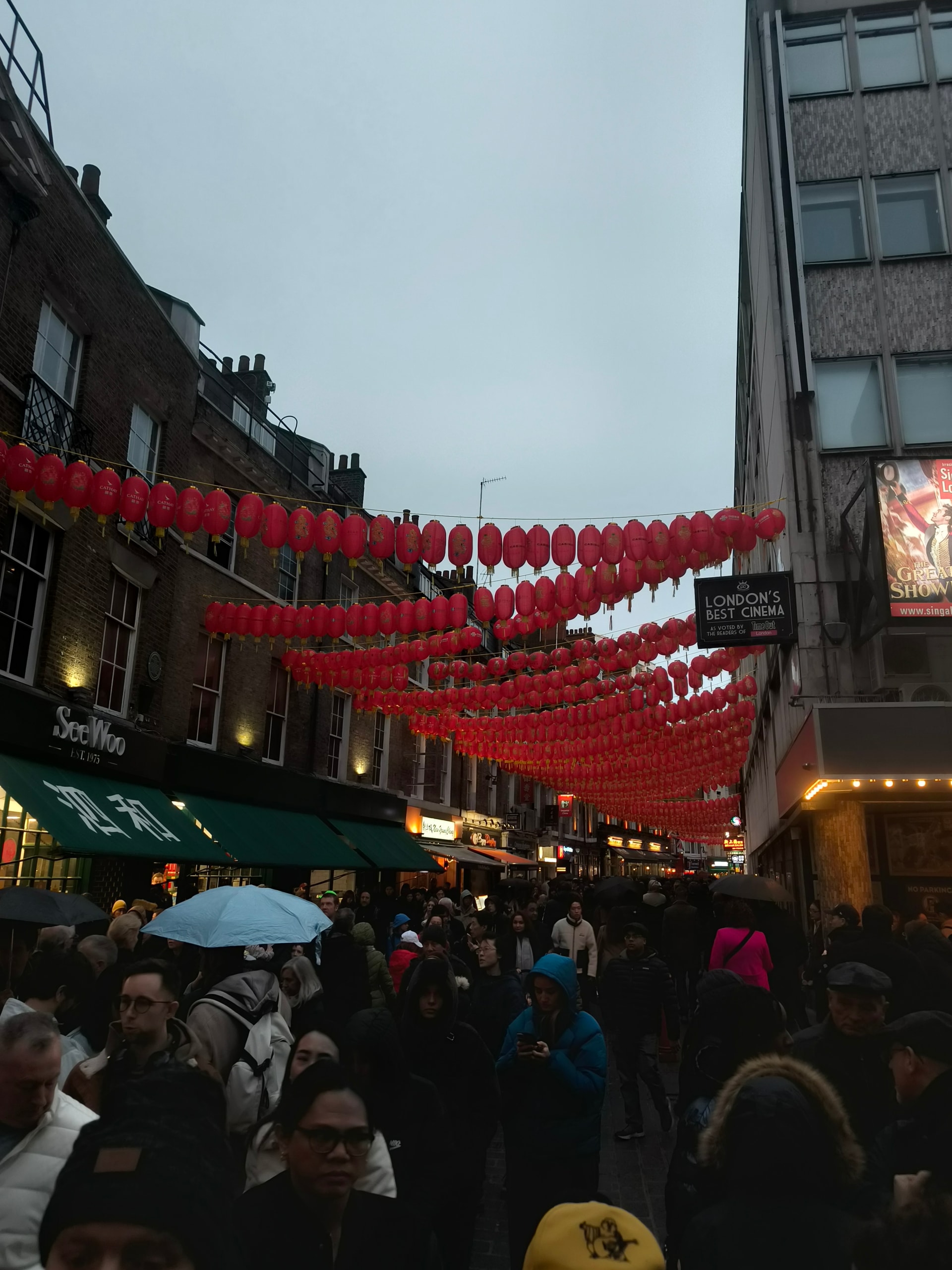 Crowded street hung with red paper lanterns between tall buildings