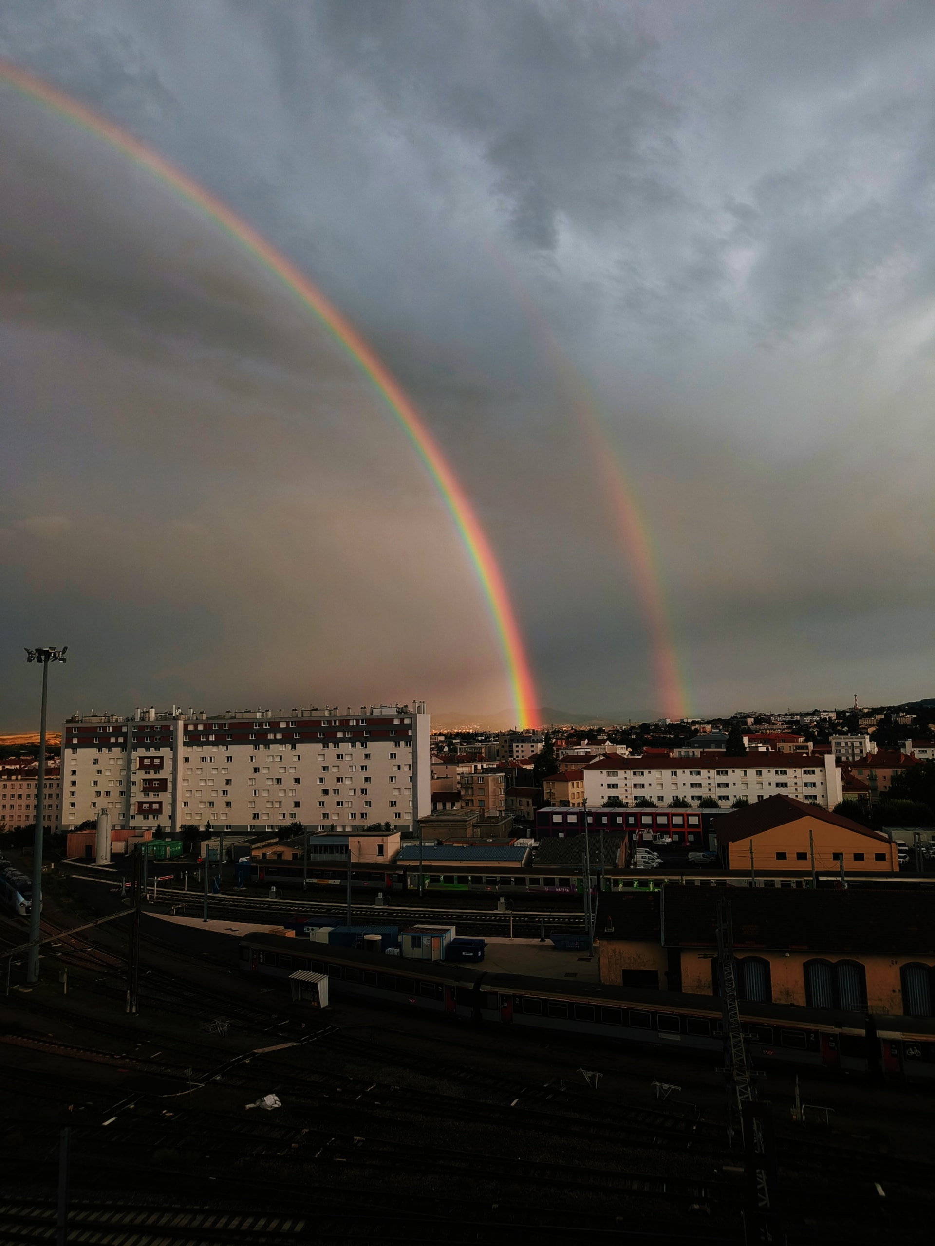 Double rainbow arching over rooftops beneath heavy storm clouds