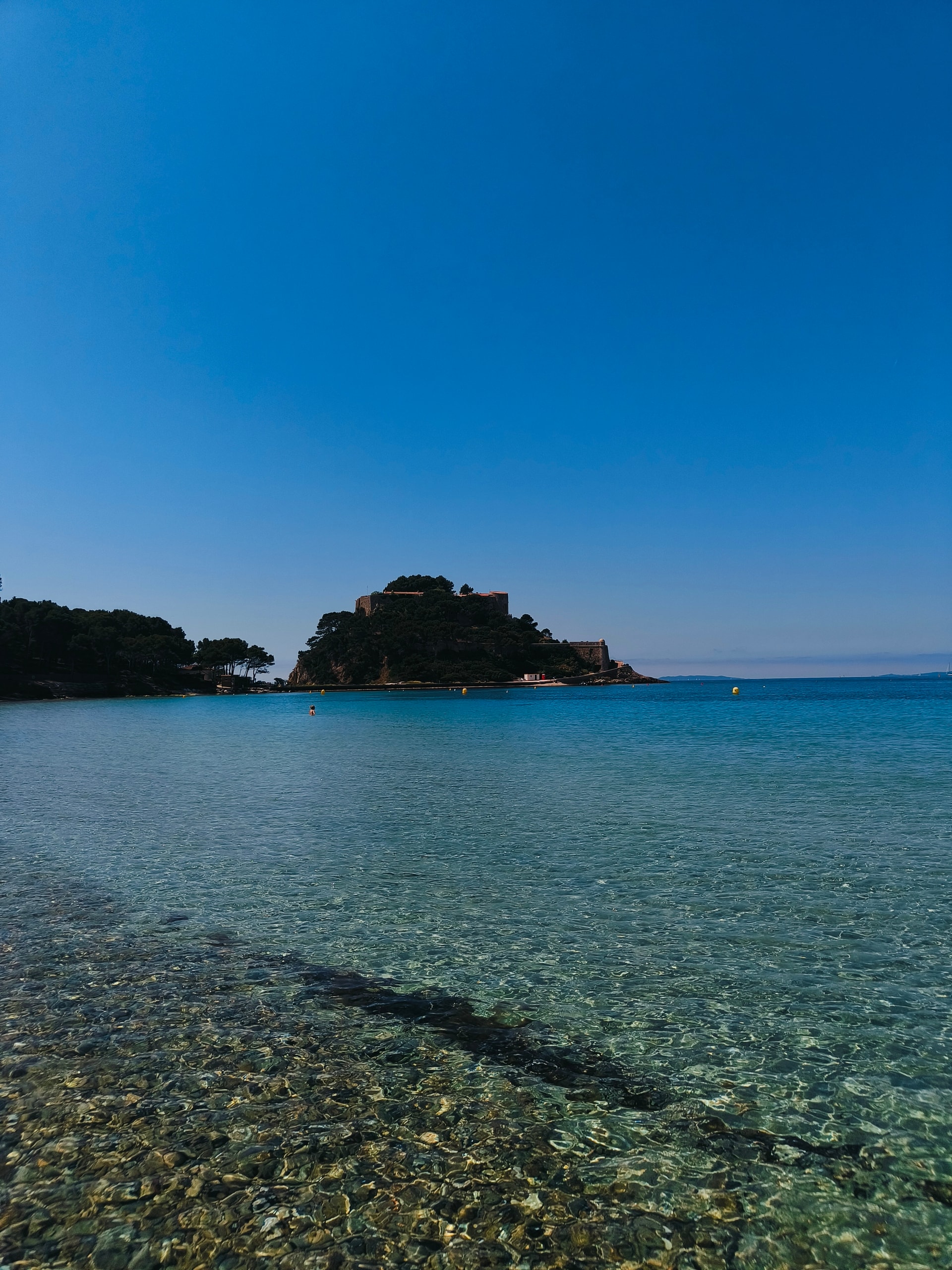 Clear shallow water over pebbles leading out to a small rocky island