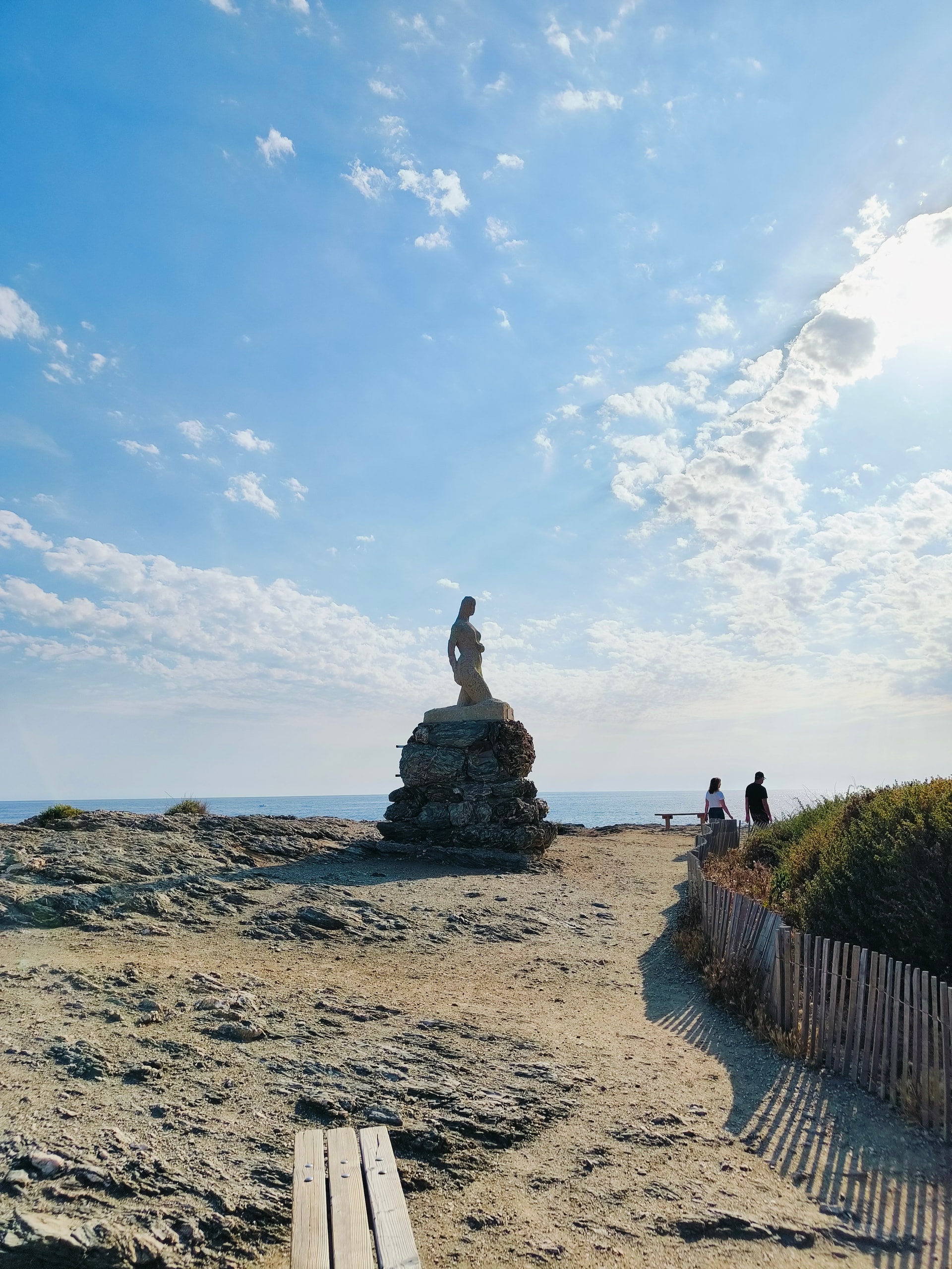 Statue on a rock at the edge of a sandy shore beside a wooden boardwalk