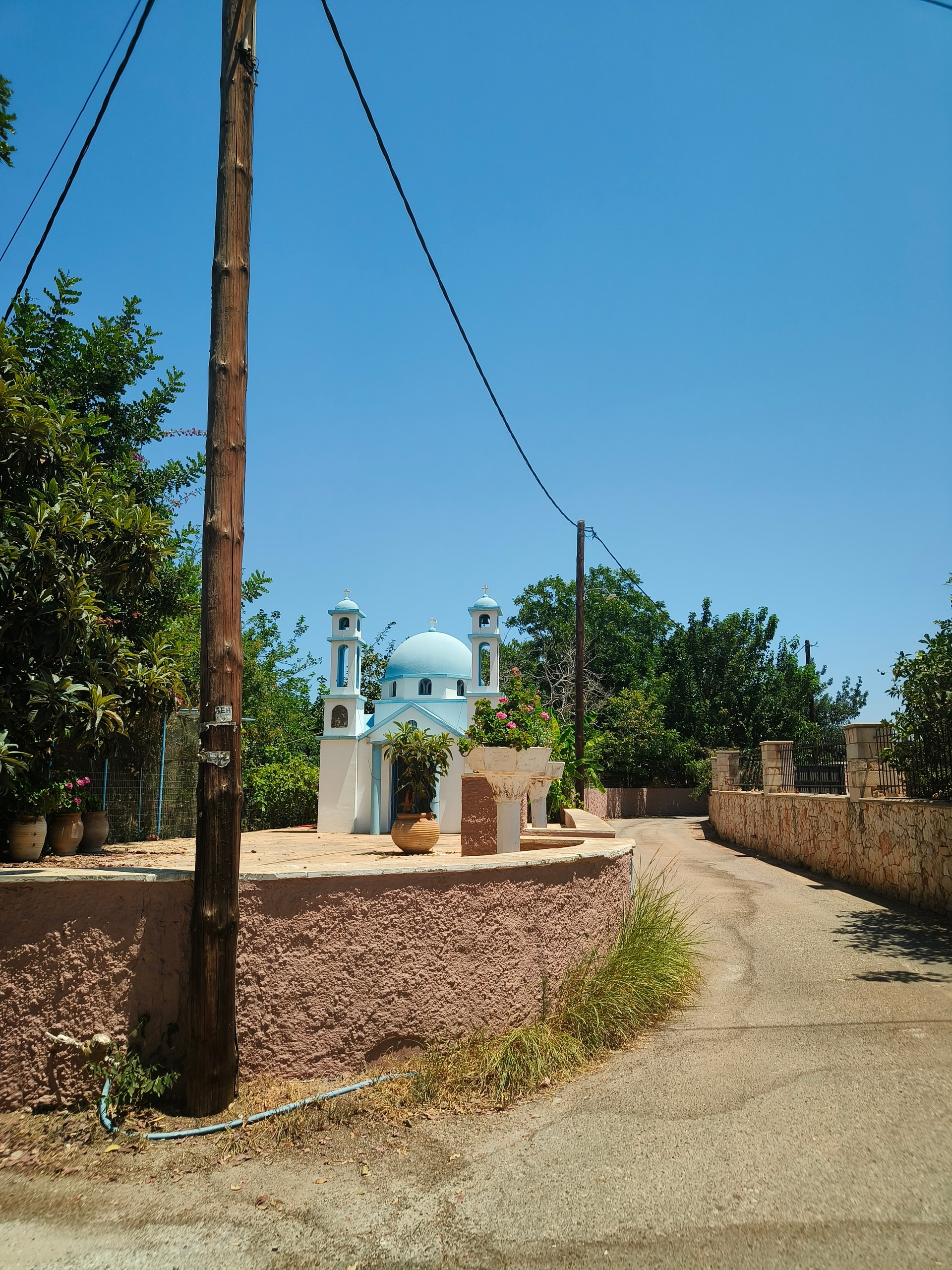 Small white chapel with blue domes beside a quiet road under a blue sky