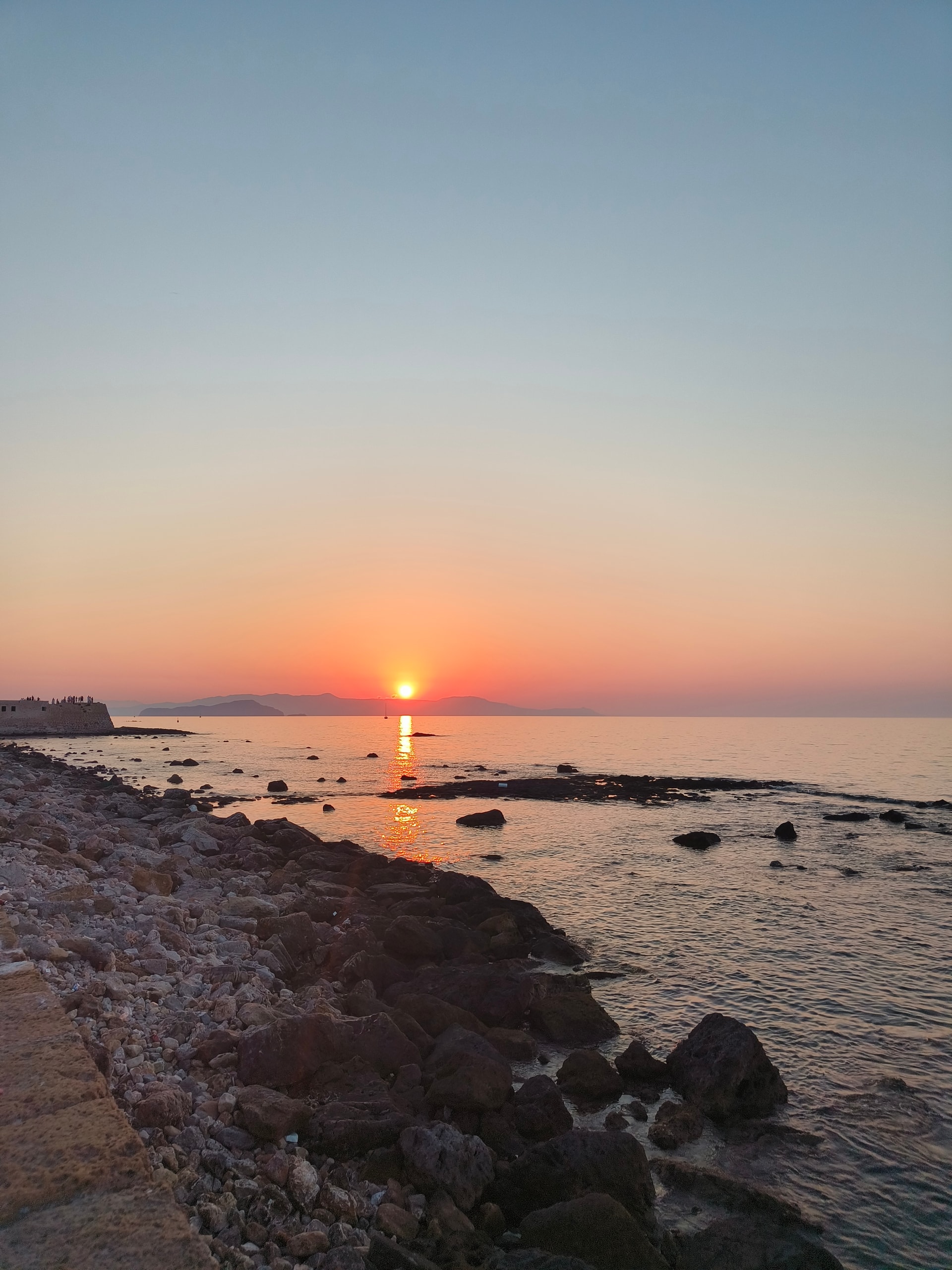 Sun setting over the sea beyond a dark rocky shore