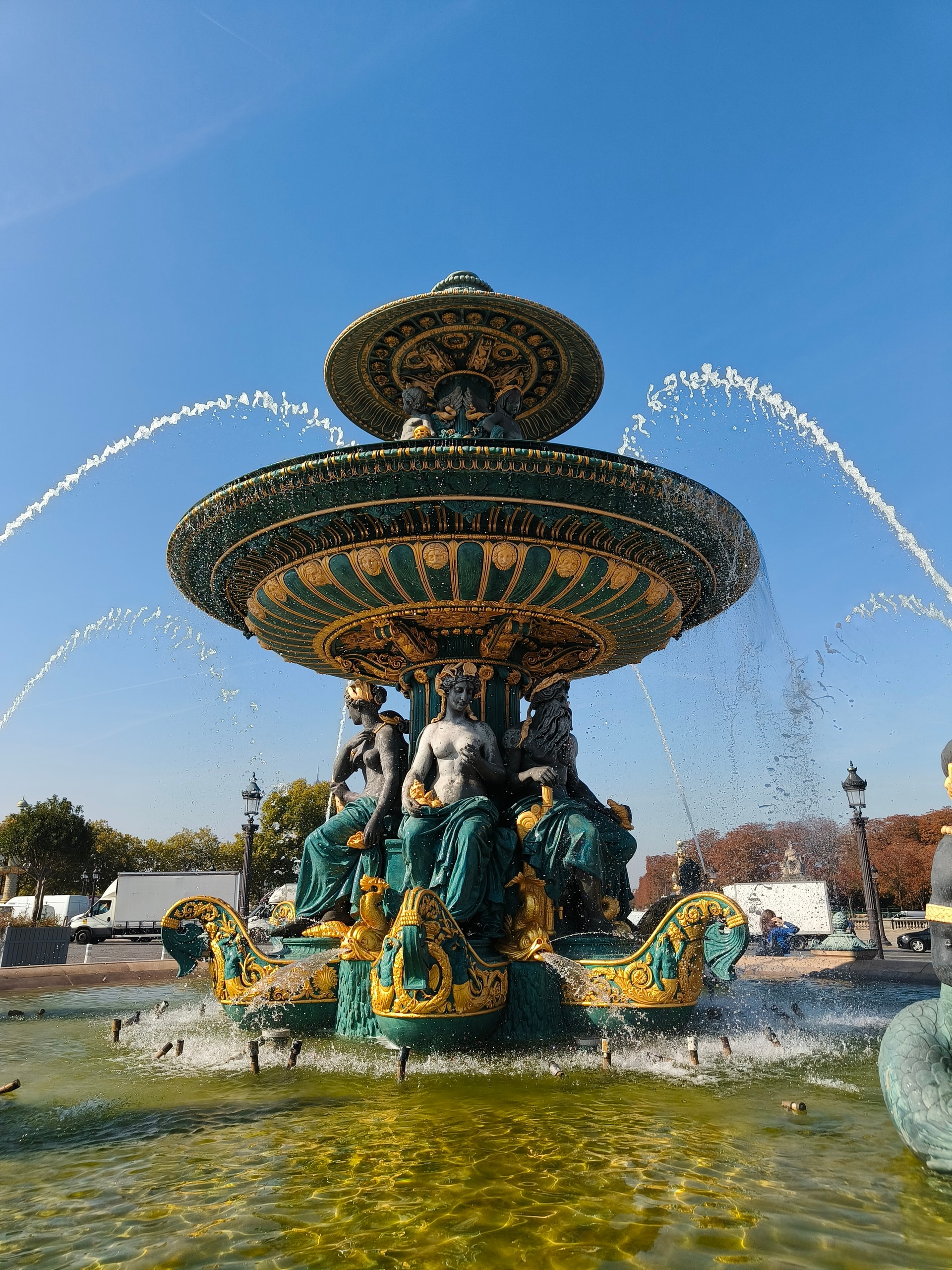 Ornate gilded fountain with bronze figures spraying water under a blue sky