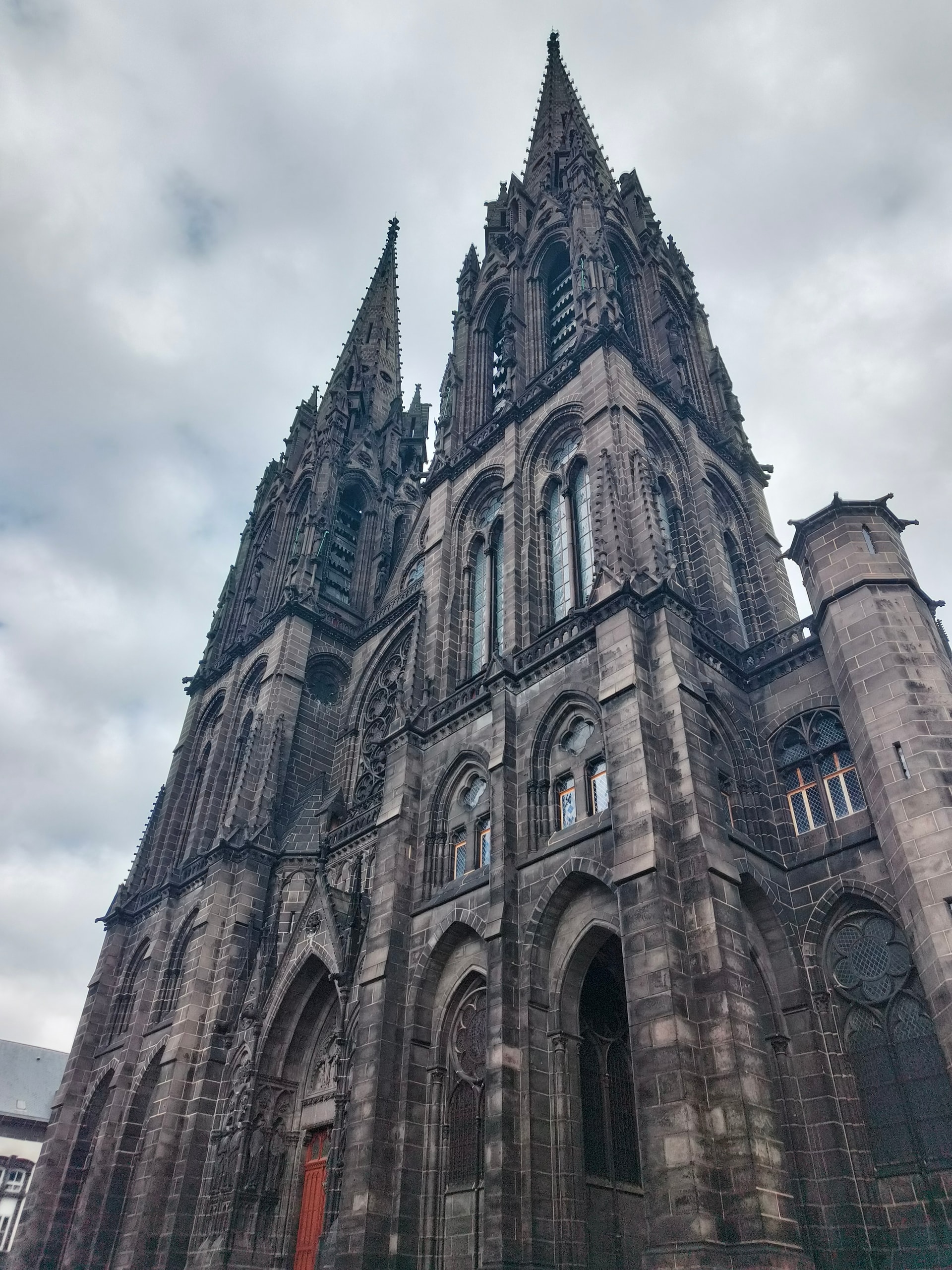 Dark stone Gothic cathedral with twin spires rising into an overcast sky