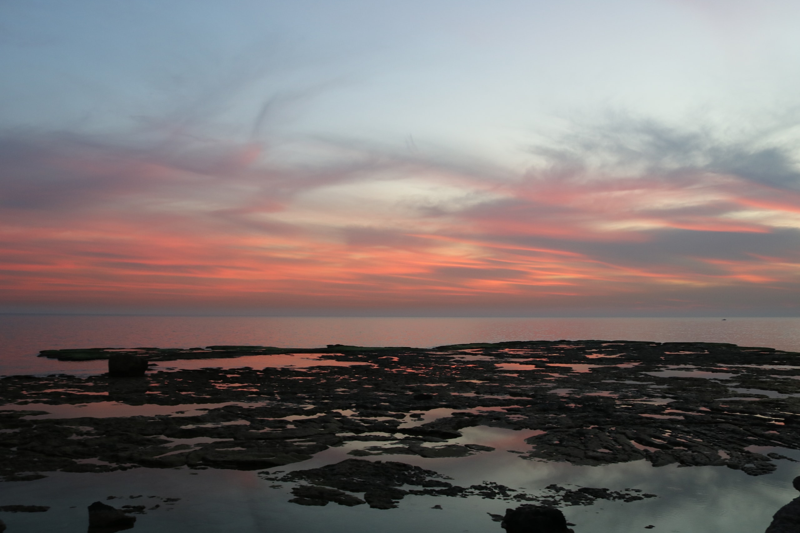 Pink and orange sunset clouds over a rocky shore scattered with tide pools