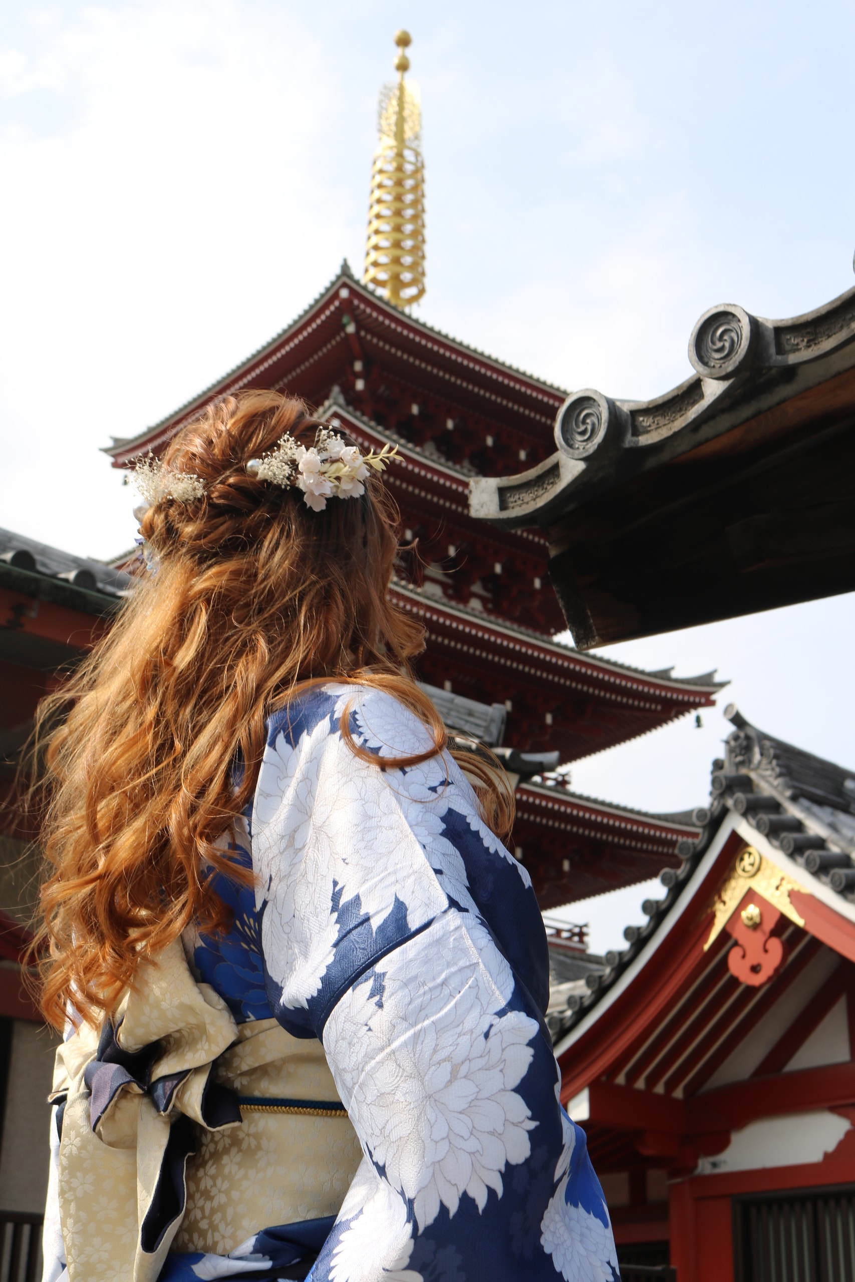 Woman with long auburn hair in a blue floral kimono facing a red five-storey pagoda