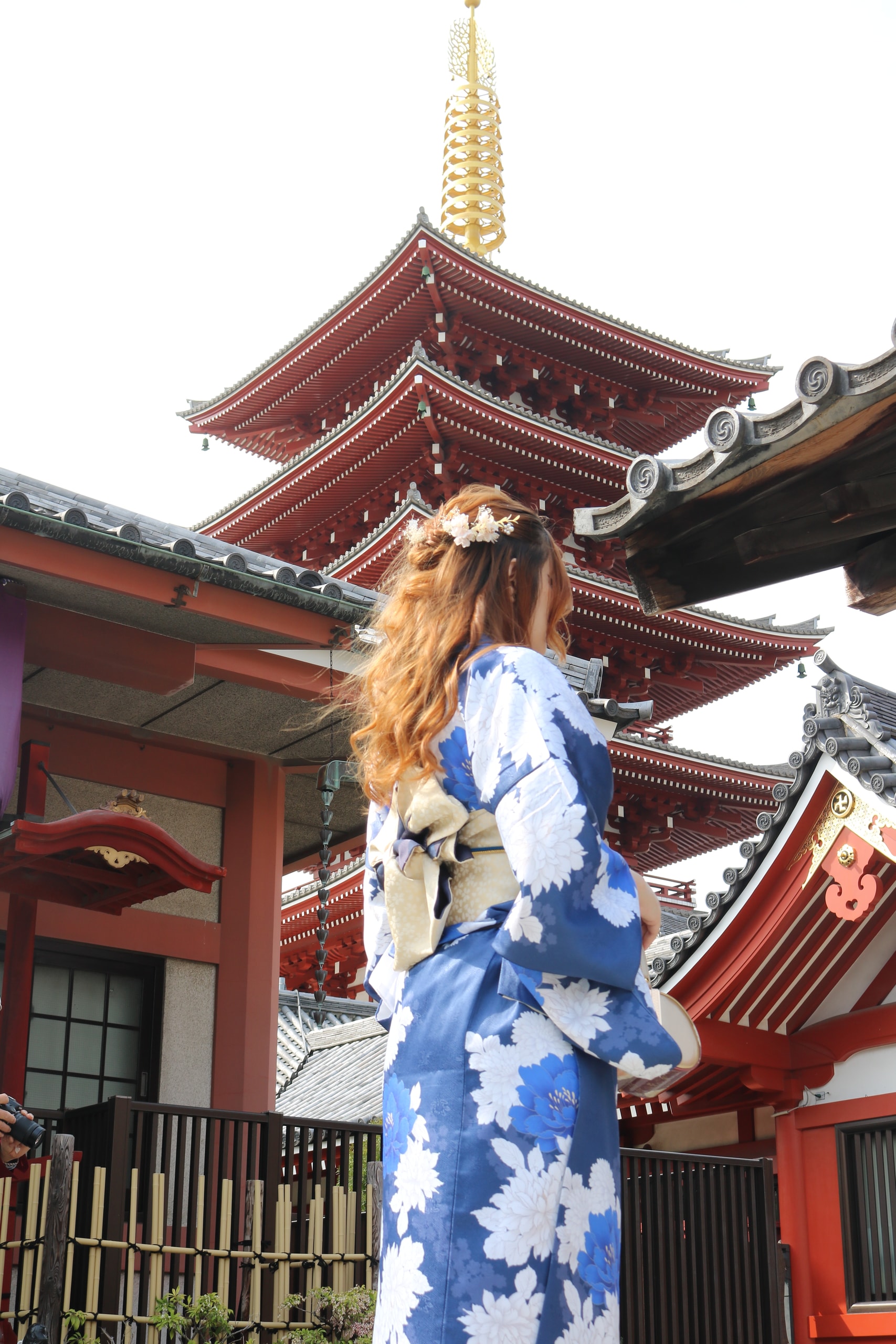 Woman in a blue floral kimono standing before a red pagoda and temple buildings