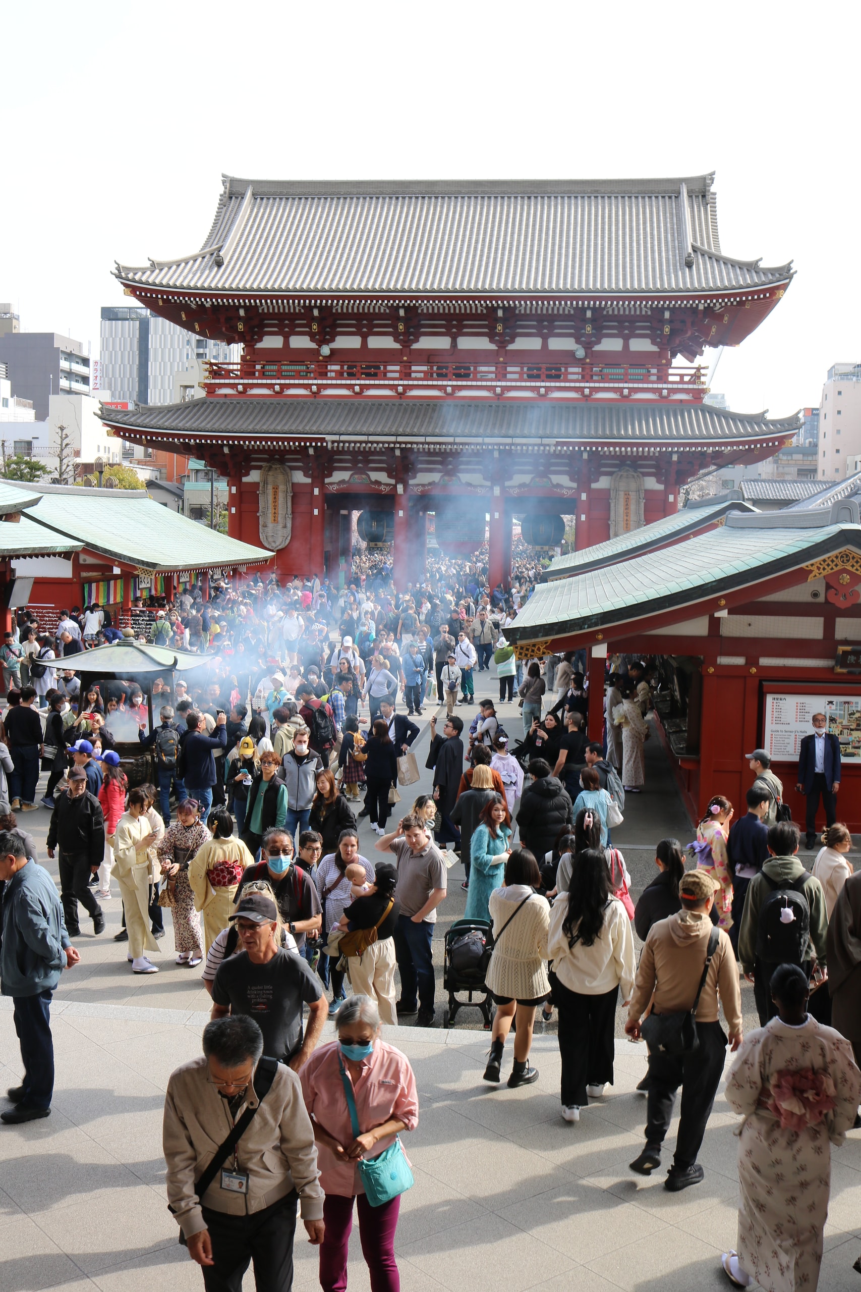 Crowds and drifting incense smoke in front of a large red temple gate