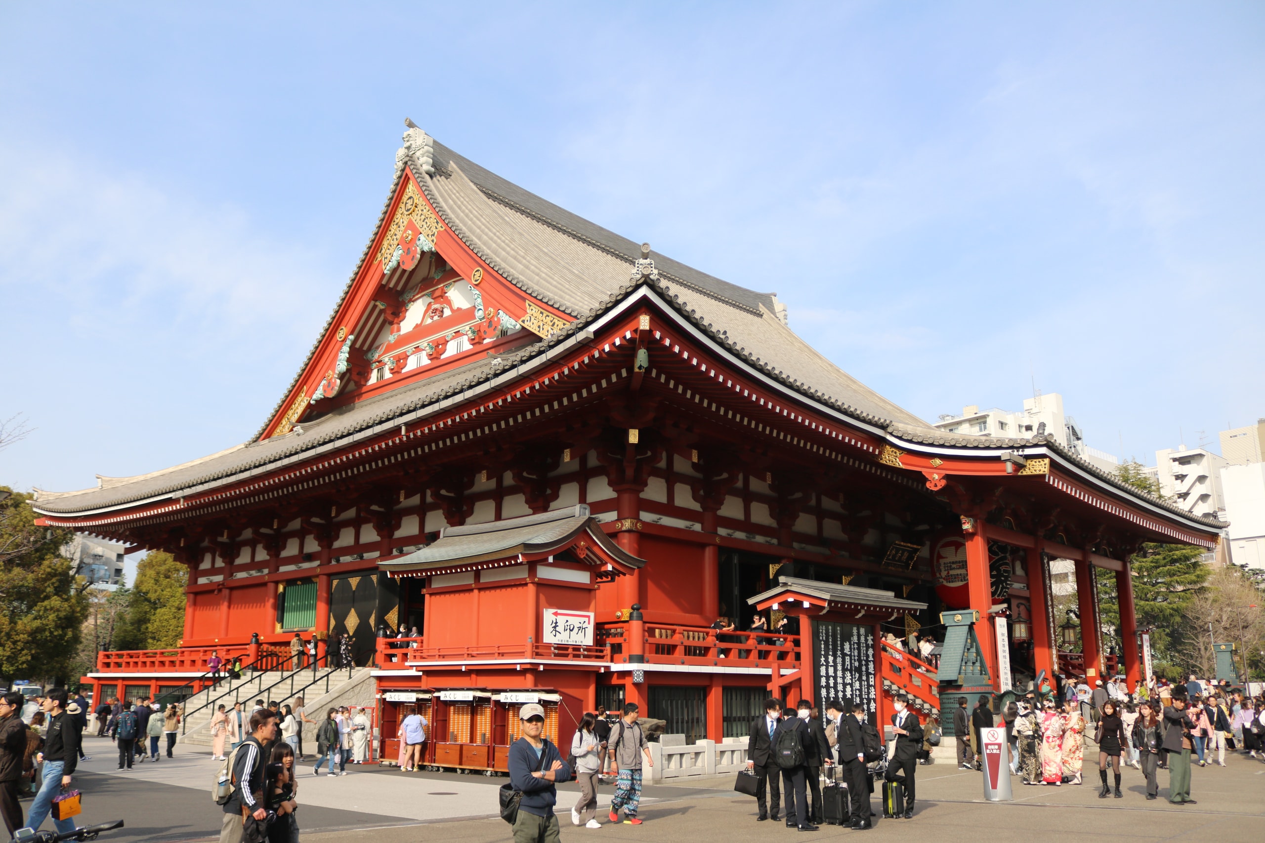Red temple main hall with visitors gathered in the square before it