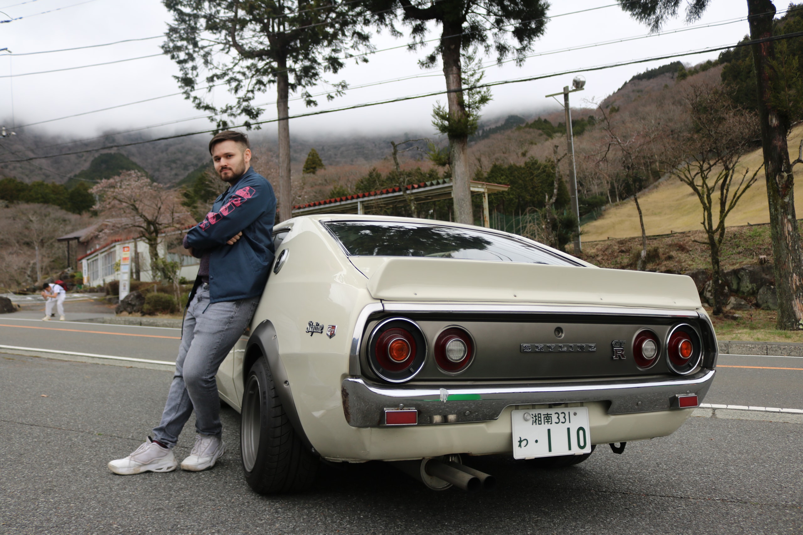 Man leaning against the rear of a white vintage sports car on a mountain road
