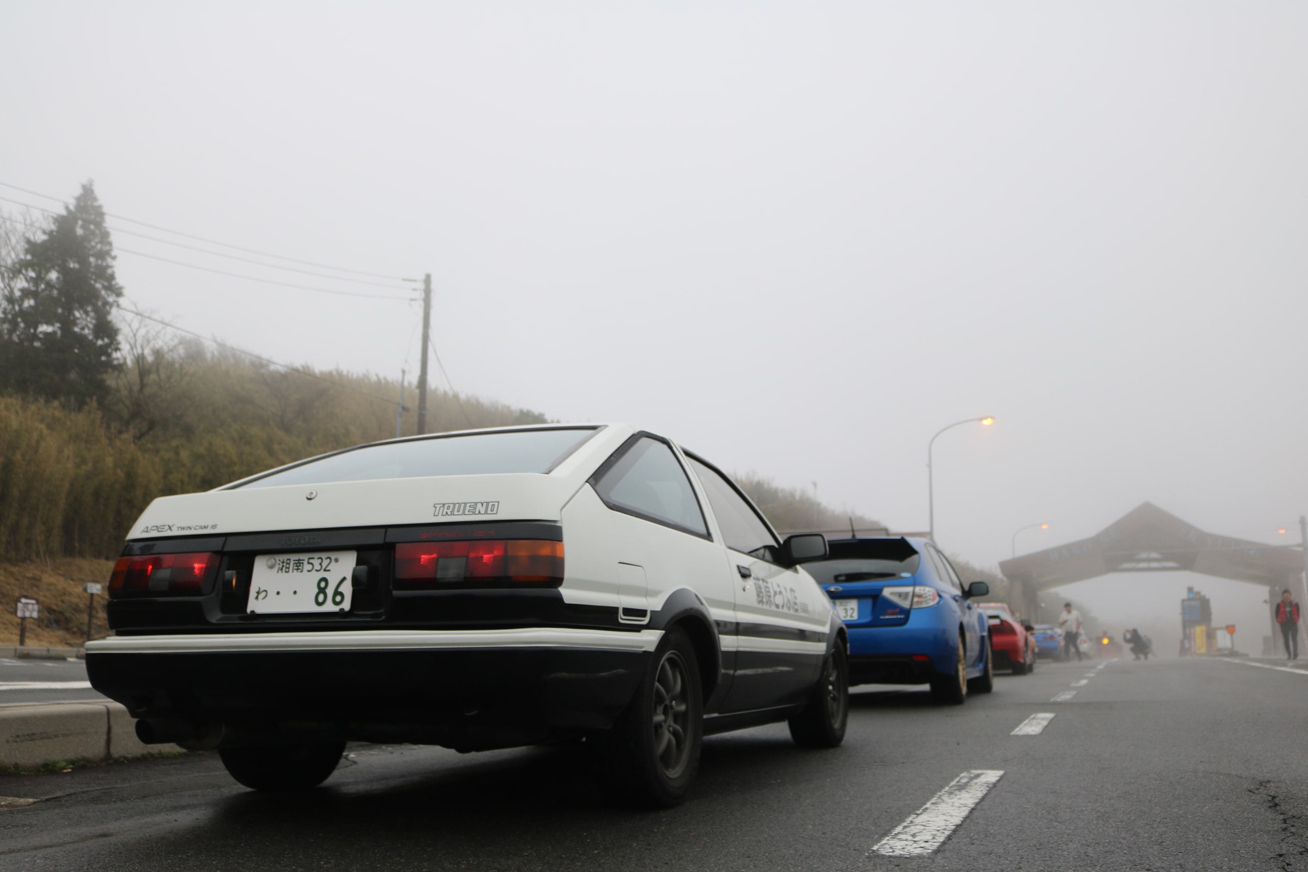 White and black 1980s coupe parked on a road disappearing into fog