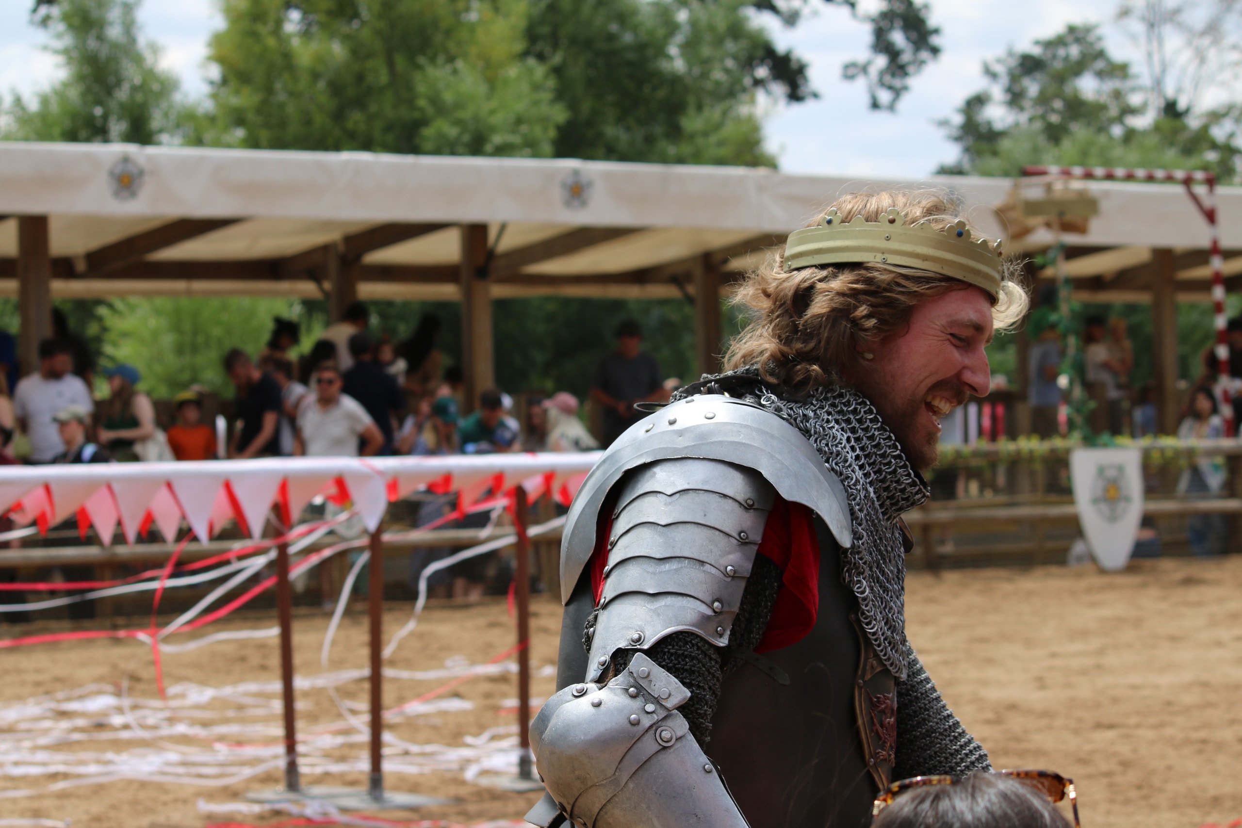 Smiling man in chainmail and plate armour at the edge of a jousting arena