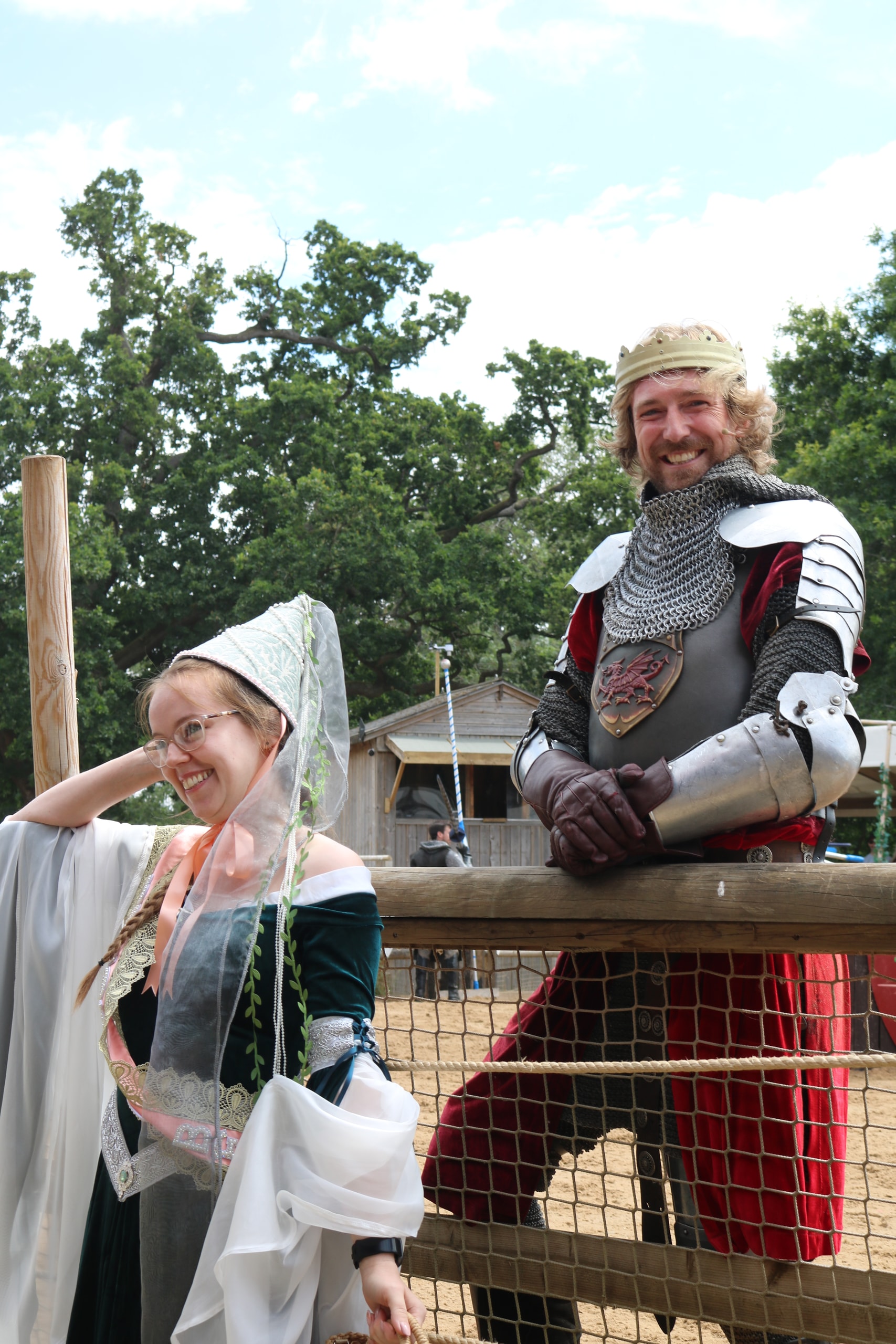 Woman in a white medieval veil and a knight in armour laughing together against a wooden fence
