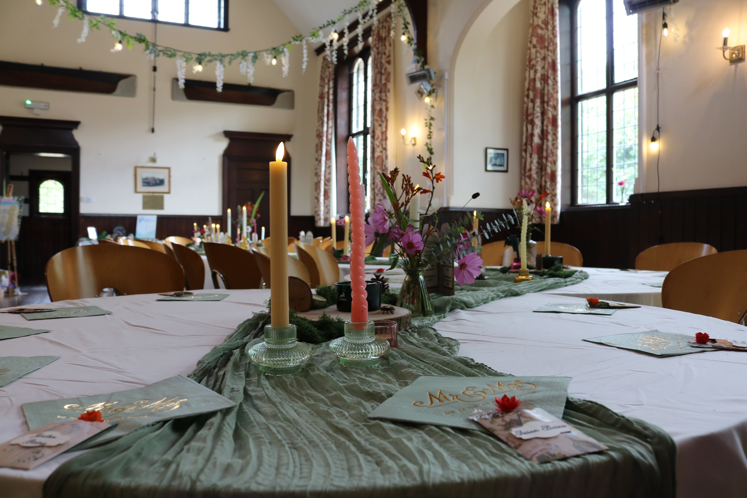 Round table dressed with a green runner, tall candles and wildflowers, garlands behind