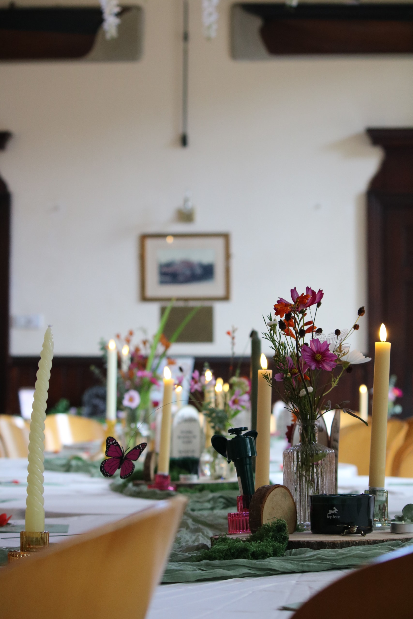 Table centrepiece of candles, wildflowers and a butterfly beneath a framed picture