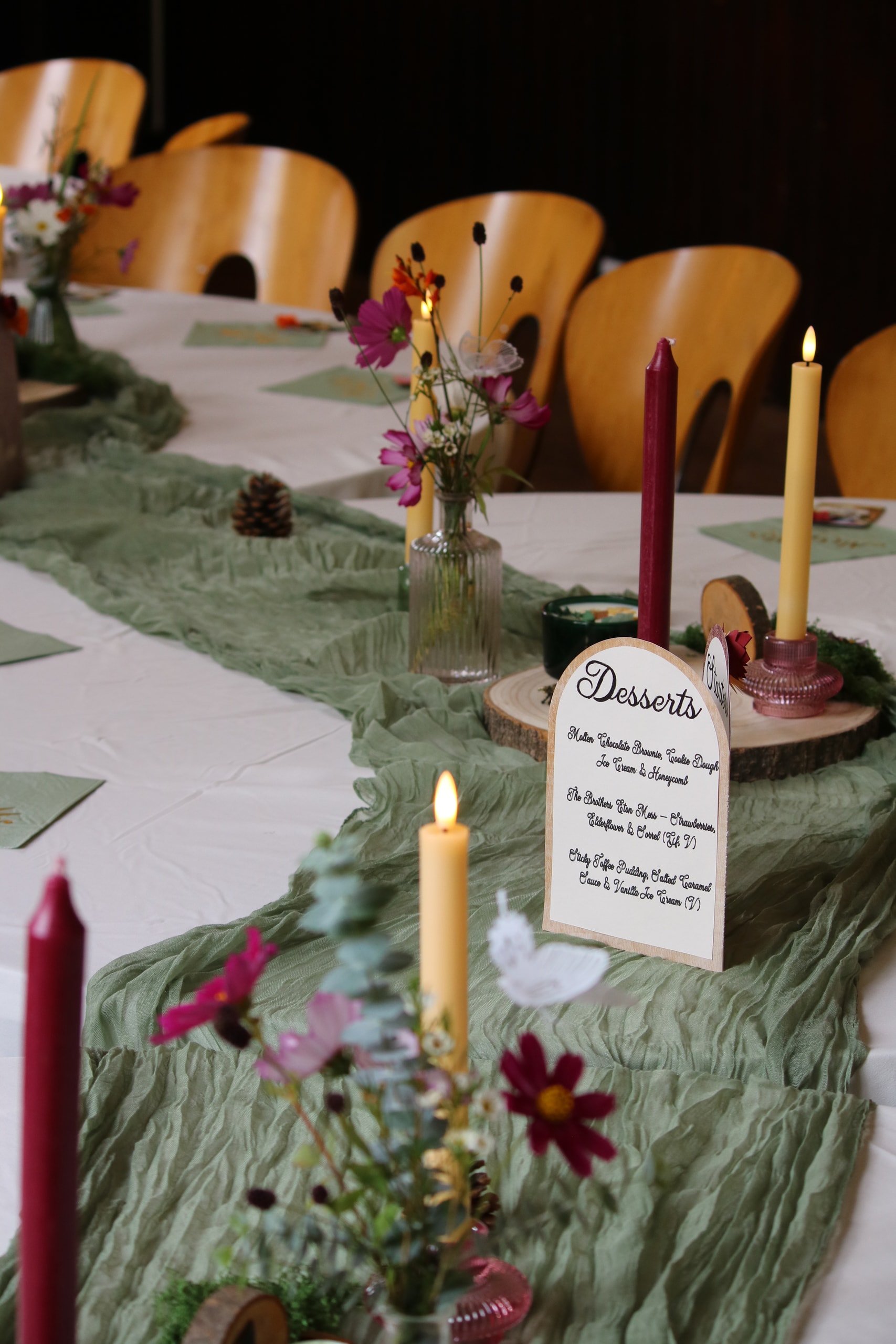 Dessert menu card among candles and flowers on a green table runner