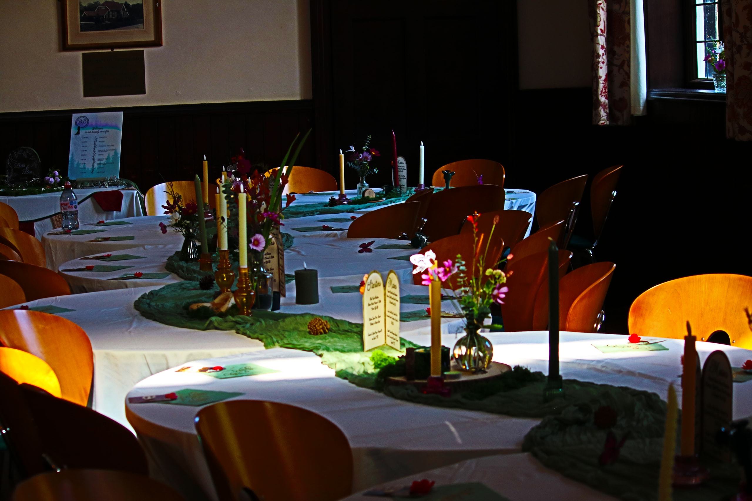 Candlelit tables with flowers on green runners in a shaded hall
